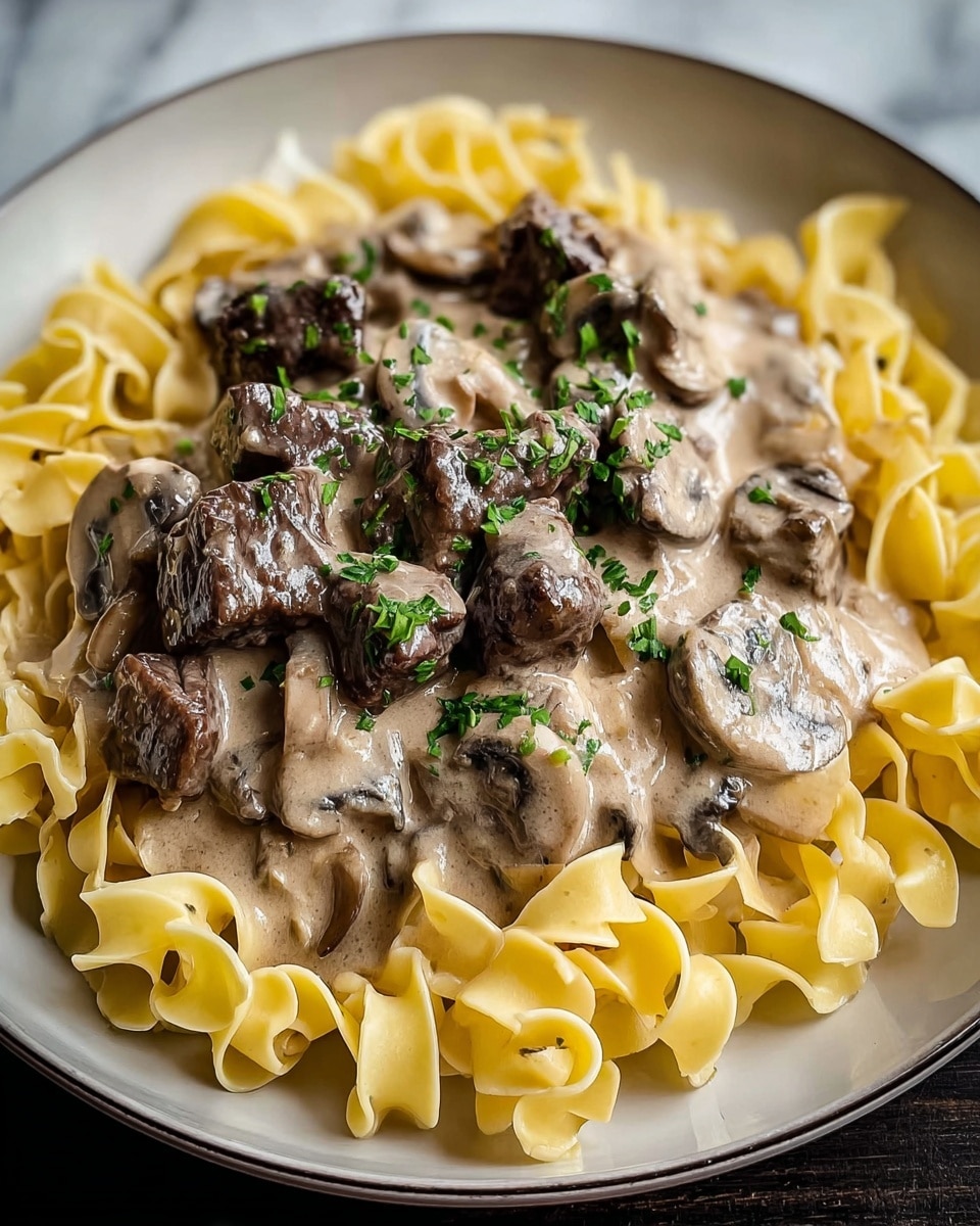 A white plate holds three main layers: the bottom layer is wide, flat, yellowish pasta ribbons arranged loosely in a circular shape; the middle layer consists of chunks of dark brown cooked beef mixed with sliced mushrooms; the top layer is a thick, creamy light beige sauce covering the beef and mushrooms, with small green herb bits sprinkled on top. The photo is taken on a white marbled surface. photo taken with an iphone --ar 4:5 --v 7