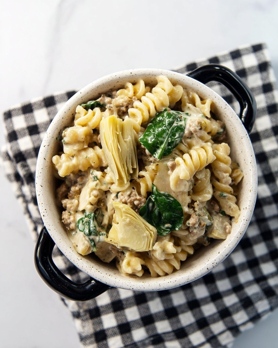A white speckled bowl with black handles sits on a black and white checkered cloth over a white marbled texture. Inside the bowl, there is a creamy pasta dish with two types of pasta: light yellow and beige rotini and a few pieces of artichoke hearts that are pale greenish-yellow. The pasta is mixed with a creamy sauce that has small bits of ground meat and herbs, giving a slightly textured look. On top, a few fresh dark green spinach leaves add a pop of color. The bowl is filled to the top, showing the rich, creamy texture of the dish. photo taken with an iphone --ar 4:5 --v 7