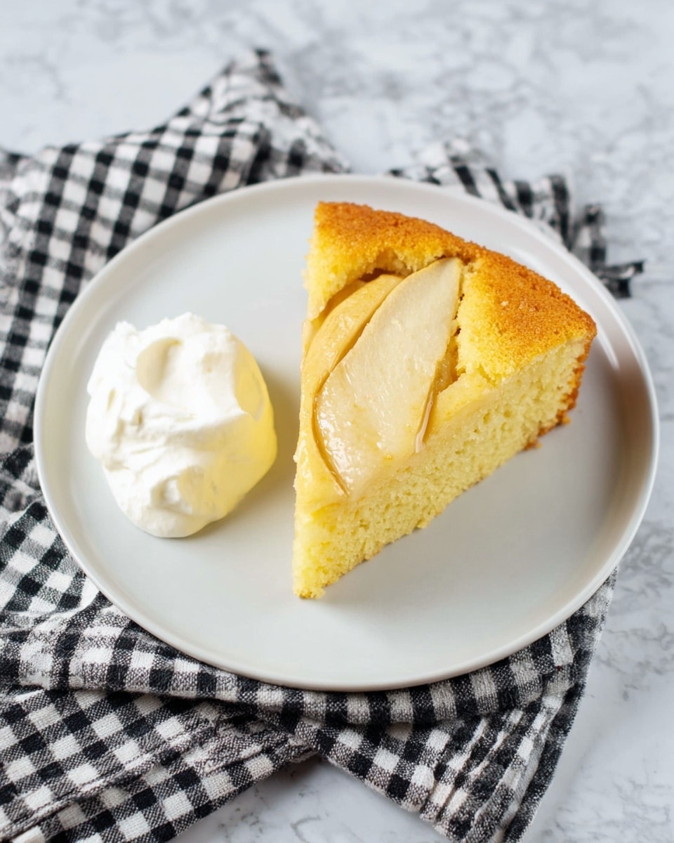 A white plate holds one slice of light yellow cake with a soft, spongy texture, featuring several thin slices of cooked apple baked into the top center. To the left of the cake slice, there is a dollop of white whipped cream with a smooth and fluffy texture. The plate is placed on a black and white checkered cloth, all set against a white marbled surface. photo taken with an iphone --ar 4:5 --v 7