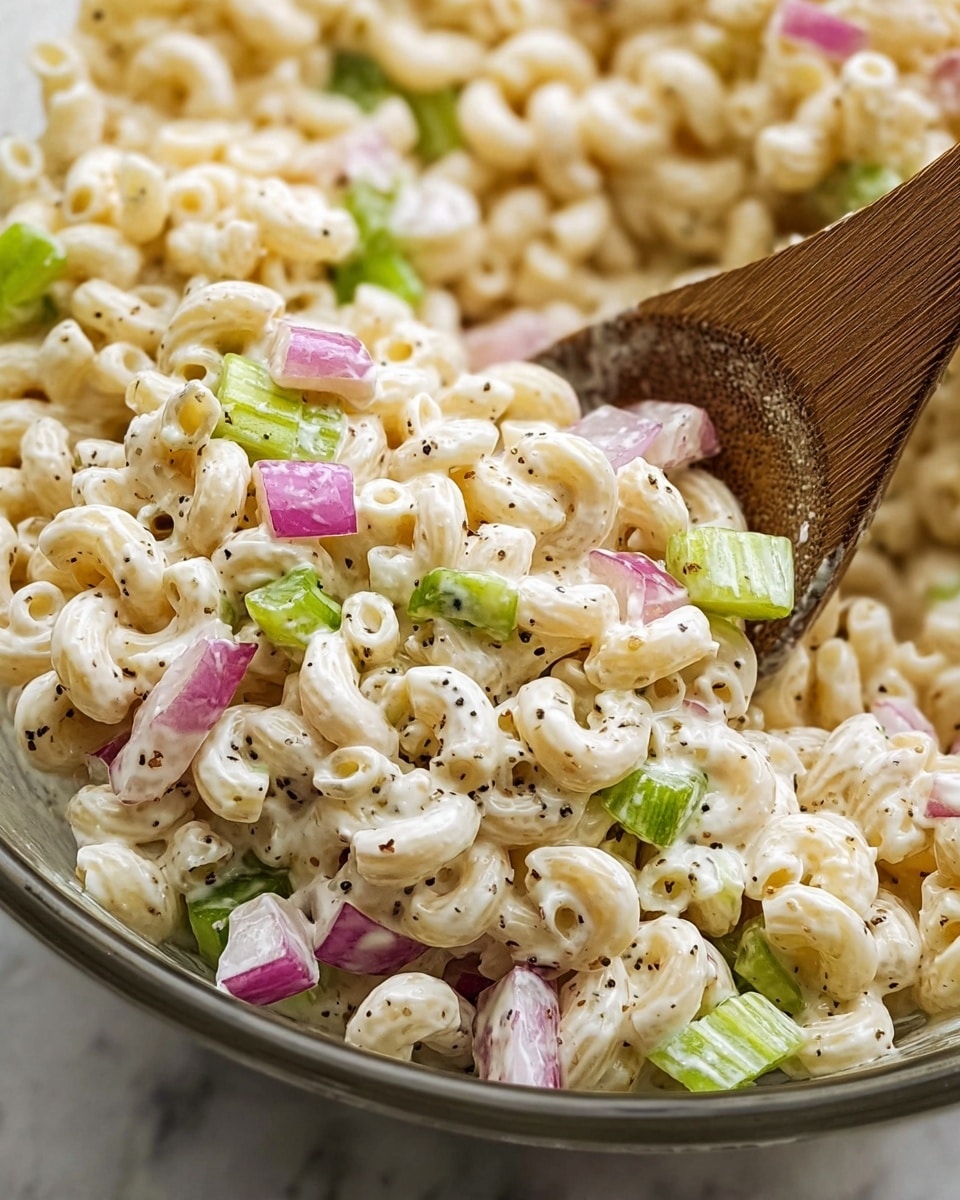 The image shows a close-up of creamy macaroni salad mixed with finely chopped red onions and bright green celery pieces, all coated in a white, thick dressing with visible black pepper specks spread throughout. The macaroni is small, curly, and pale yellow, creating a soft and smooth texture. A wooden spoon is partially visible on the right side, stirring the salad, with a woman's hand holding it. The salad sits on a white marbled surface. photo taken with an iphone --ar 4:5 --v 7