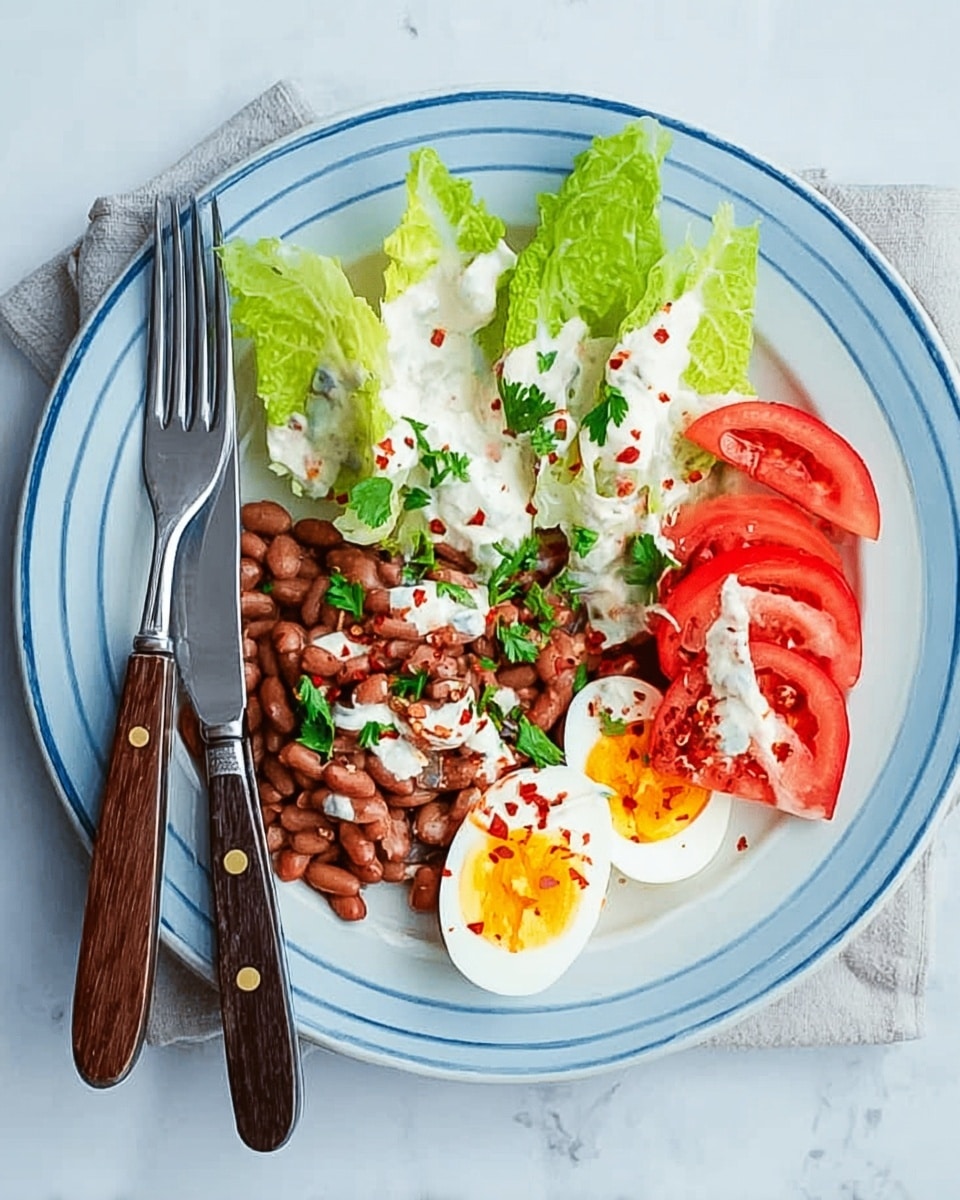 A white plate with a thin blue rim holds a fresh salad arranged in a neat layout on a white marbled surface. At the top left, three small wedges of green romaine lettuce are lightly drizzled with a creamy white dressing. Below and to the right of the lettuce, there is a mix of brown beans scattered over a bed of creamy sauce, with small green parsley leaves and a few red pepper flakes sprinkled on top. At the bottom left, quartered red tomatoes are placed in a small cluster. On the right side of the plate, two halves of a boiled egg show a bright yellow yolk in the center, garnished with a small parsley leaf and red pepper flakes. A fork with a dark wooden handle is on the left side of the plate, and a knife with a matching handle is on the right side. The whole setting rests on a soft blue cloth napkin. Photo taken with an iphone --ar 4:5 --v 7