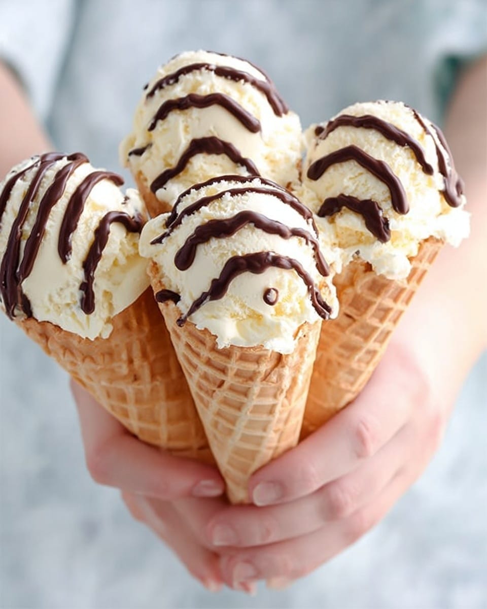 The image shows two ice cream cones held by a woman's hand, each with a single scoop of creamy white ice cream topped with dark brown chocolate drizzle shaped in thin lines. The waffle cones are light golden brown with a visible textured pattern. In the background, slightly blurred, there are more ice cream cones held by another woman's hand. The background is soft blue, and the surface beneath is a white marbled texture. Photo taken with an iphone --ar 4:5 --v 7