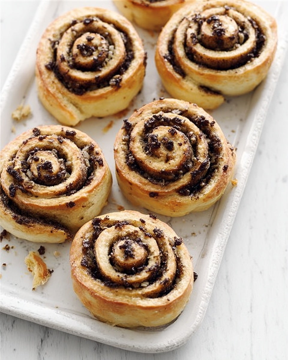 The image shows six cinnamon rolls placed on a white rectangular plate, all arranged unevenly with some closer together and others slightly apart. Each roll has a light golden-brown outer layer with a slightly crispy texture, while the inner swirls are darker brown with visible specks of cinnamon and sugar, creating a spiraled pattern. The rolls have a soft, fluffy appearance with some flaky bits on top, and small crushed pieces scattered around the plate. The setting features a white marbled textured surface underneath the plate. photo taken with an iphone --ar 4:5 --v 7
