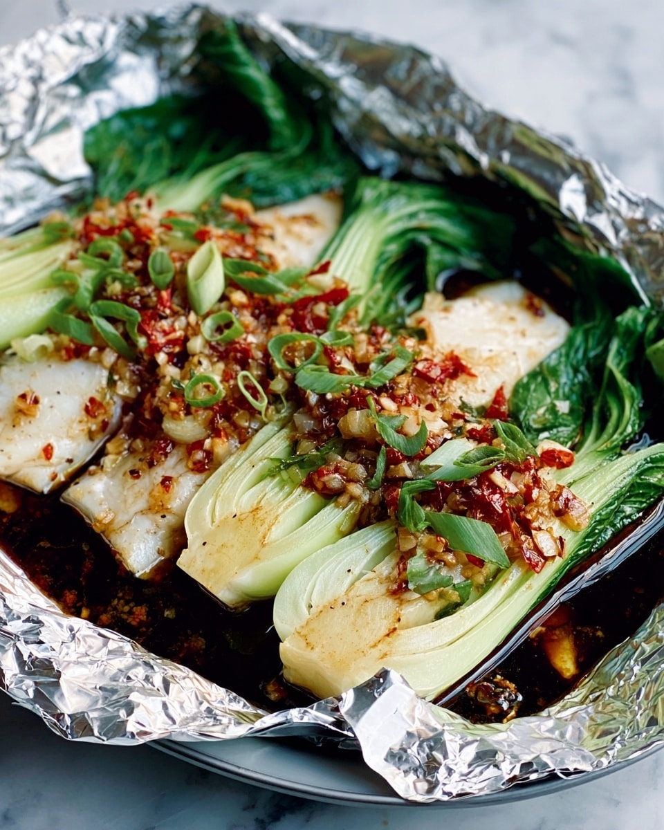 The image shows a dish made with three main layers placed on a sheet of crinkled silver foil. The bottom layer contains fish fillets topped with a thick sauce made of finely chopped garlic and red chili pieces, giving a mix of pale yellow and red colors. On top and around the fish, there are several baby bok choy leaves with bright green leafy tops and white crunchy stems, arranged to cover most parts. The foil rests on a black round plate, and the background is a white marbled surface. The bright colors and shiny textures make the food look fresh and tasty. photo taken with an iphone --ar 4:5 --v 7
