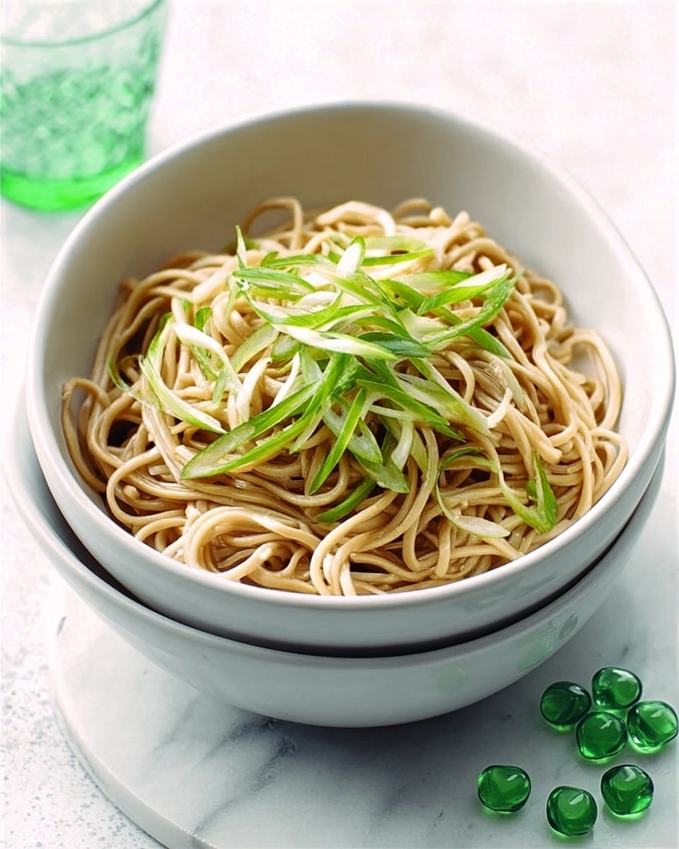A white bowl is stacked inside another white bowl, both placed on a white marbled surface. Inside the top bowl, there is a neat pile of light brown noodles with some long, thin green vegetable strips scattered on top. The noodles look soft and slightly glossy, while the green strips add a fresh and crisp touch. Soft natural light shines from one side, casting gentle shadows and highlighting the textures of the noodles and vegetables. photo taken with an iphone --ar 4:5 --v 7