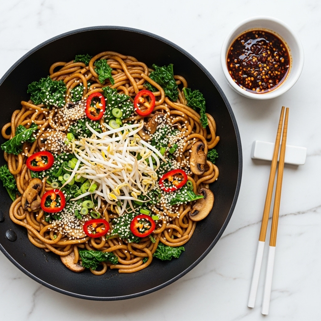 A black pan filled with a dish of thick, light brown noodles mixed with dark green kale leaves and sliced light beige mushrooms, garnished with thin slices of red chili peppers, chopped light green scallions, white sesame seeds, and white bean sprouts layered on top. Next to the pan are wooden chopsticks resting on a white chopstick holder, and a small white bowl containing dark brown sauce with red chili flakes. All items are placed on a white marbled surface. Photo taken with an iphone --ar 4:5 --v 7