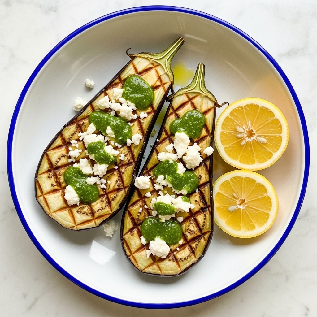 The dish shows two halves of grilled eggplants placed side by side in a white bowl with a blue rim. Each eggplant half has a crosshatch pattern on the golden-brown cooked surface. A green herb sauce is spread along the top side of both pieces, with white crumbled cheese sprinkled over them. To the right side of the eggplants, there is a half lemon with a bright yellow color. The green sauce partially pools around the edges of the eggplants, creating a fresh contrast against the white bowl and white marbled surface underneath. photo taken with an iphone --ar 4:5 --v 7