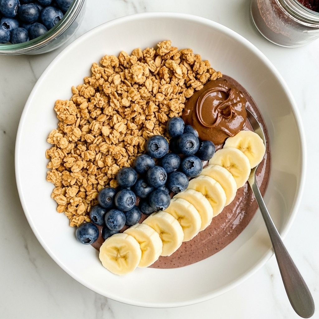 A white bowl contains three main layers arranged in a neat circle: the bottom layer is crunchy brown granola with nuts and seeds, the middle layer shows a row of dark purple blueberries placed close together, and the top layer has a dollop of dark brown chocolate or nut butter in the center. On one side of the bowl, there are five thick slices of pale yellow banana neatly lined up. A metal spoon rests on the edge of the bowl which is on a white marbled surface. In the top left corner, there is a clear container with more blueberries, and in the top right corner, a jar or bowl with more chocolate spread is partially visible. photo taken with an iphone --ar 4:5 --v 7