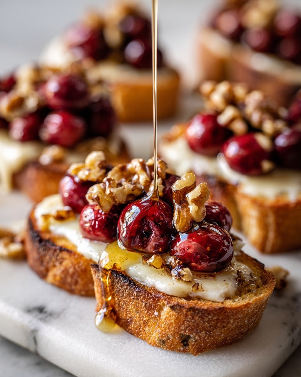 The image shows several small open-faced toasts arranged closely on white parchment over a white marbled surface. Each toast has three visible layers: at the bottom, a thick slice of golden-brown crusty bread with a rough texture; in the middle, a smooth, creamy white slice of cheese covering the bread; on top, bright red roasted cherries, some with a shiny, slightly wrinkled skin, sprinkled with small pieces of chopped nuts and tiny green herbs. A thin stream of golden honey is being drizzled over the cherries on the closest toast. The focus is sharp on the front toasts and softens in the background. Photo taken with an iphone --ar 4:5 --v 7