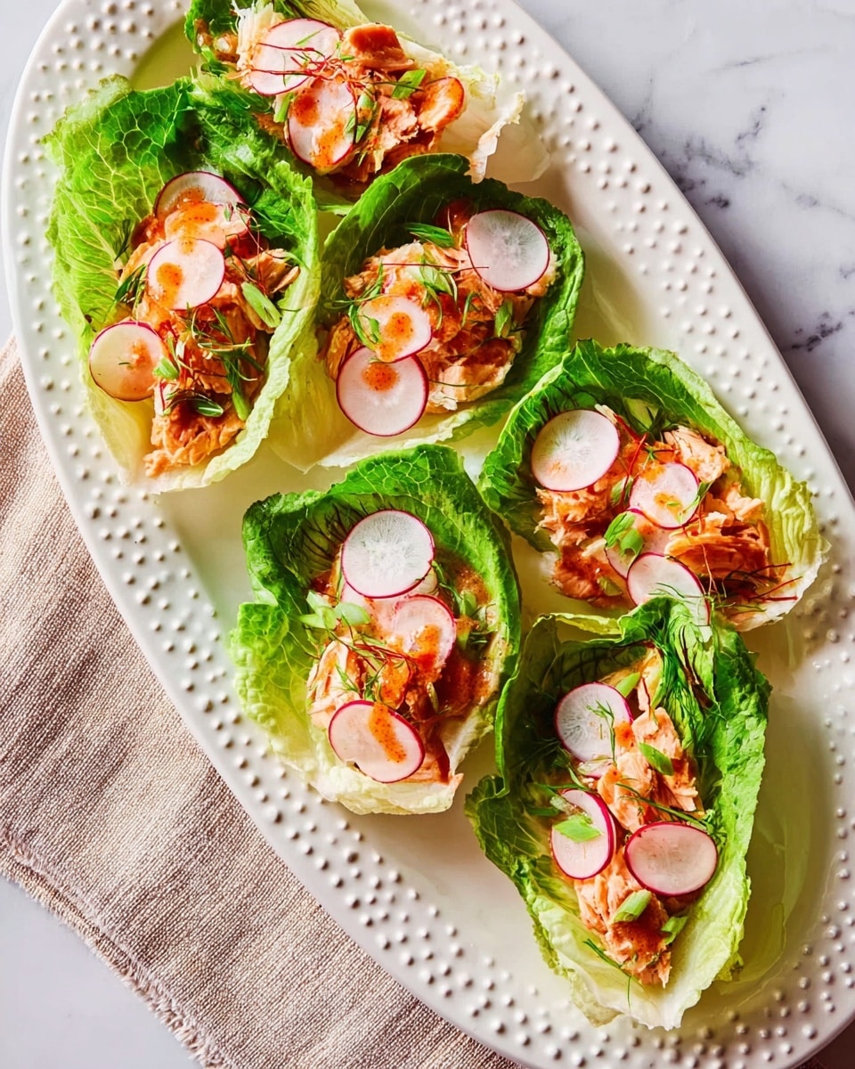 The image shows five lettuce wraps arranged on a large white oval plate. Each wrap consists of a bottom layer of green leafy lettuce, topped with slices of orange and white vegetables, followed by pieces of light pink cooked chicken. Thin, round slices of radish with white centers and pink edges lay on top of the chicken, with a drizzle of reddish sauce and a sprinkle of green herbs scattered over everything. The plate is placed on a soft pink cloth with fringed edges, all set on a white marbled surface. photo taken with an iphone --ar 4:5 --v 7