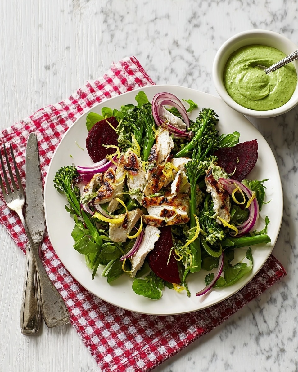 A plate holds a fresh salad with several layers: at the bottom are thin, dark red strips of beetroot and light purple slices of onion; on top, there are bright green leafy vegetables and broccoli florets scattered around. Grilled chicken pieces with a slightly charred texture are spread evenly across the salad, topped with light yellow lemon zest curls and a few small green basil leaves. Next to the plate, a white bowl contains a smooth, bright green dip with a spoon inside. The plate and bowl sit on a red and white checkered cloth over a white marbled surface. Photo taken with an iphone --ar 4:5 --v 7
