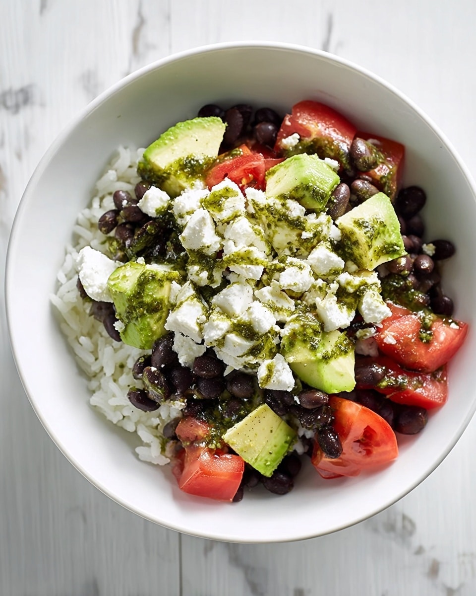 This dish is served in a white bowl and has three main layers. The bottom layer is white rice, topped with a layer of whole black beans that cover most of the rice. On top, there are medium-sized chunks of bright green avocado and juicy red tomato pieces, evenly spread. Small white crumbles of cheese are scattered over the top, and there is a green sauce drizzled lightly across the dish. The bowl sits on a white marbled surface. photo taken with an iphone --ar 4:5 --v 7