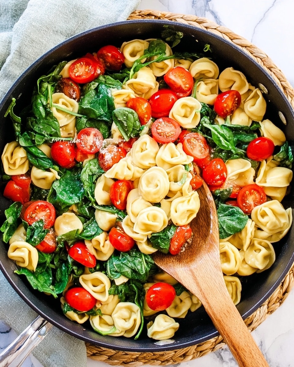 A close-up view of a black pot filled with three main layers: the bottom layer is light yellow tortellini pasta with a smooth and slightly shiny texture; the middle layer is bright green cooked spinach, wilted but still vibrant with a slightly soft texture; the top layer consists of small, glossy, bright red cherry tomatoes scattered evenly throughout. A wooden spoon is lifting some of the mix, showing the combination of tortellini, spinach, and tomatoes together. The pot sits on a white marbled surface with a woven mat and a grey cloth partially visible at the edges. photo taken with an iphone --ar 4:5 --v 7