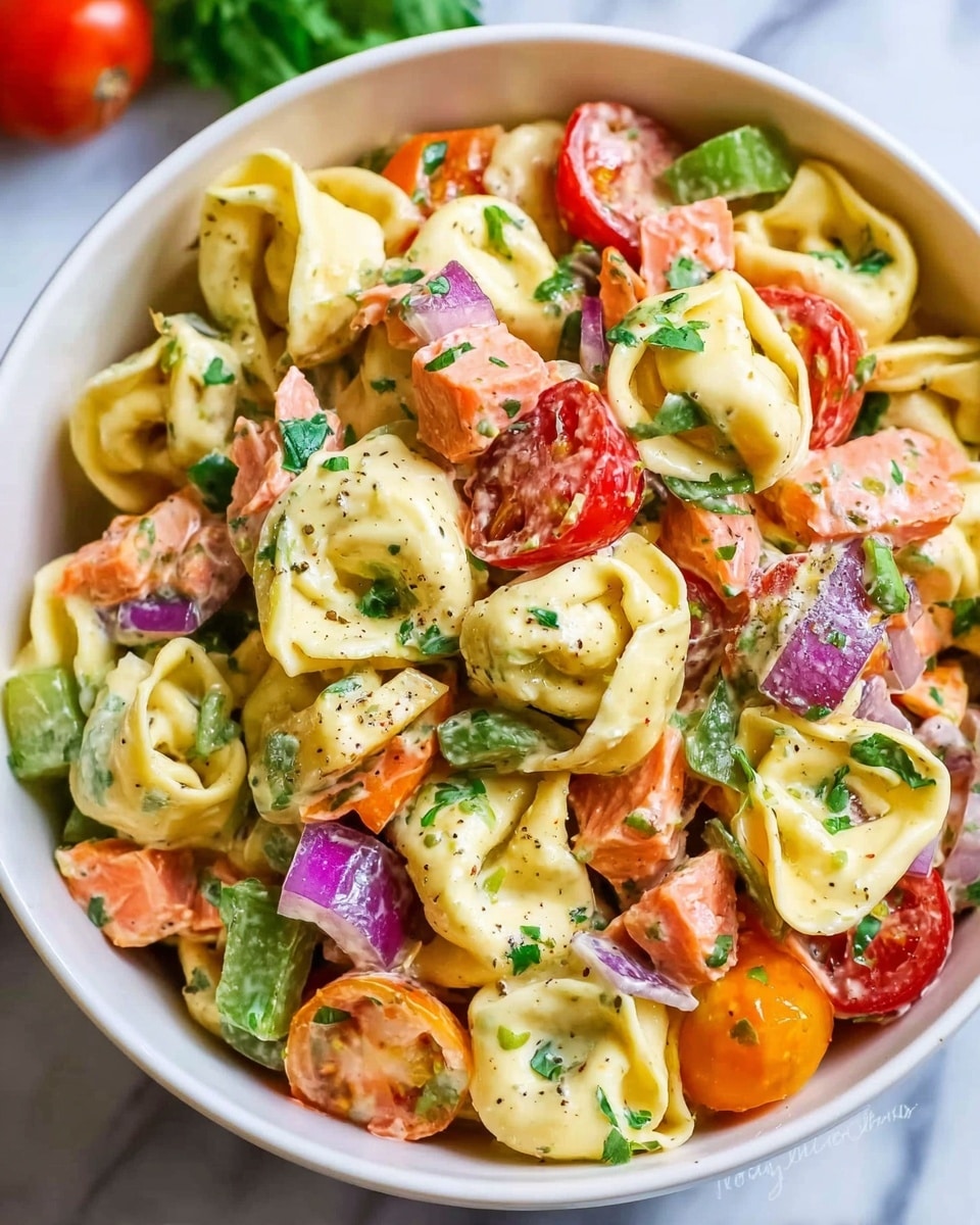 A close-up of a white bowl filled with creamy tortellini pasta salad, showing three clear layers: the top layer is scattered with chopped fresh green herbs and pieces of red and green bell peppers, the middle layer is made of creamy yellow tortellini pasta, and the bottom layer contains chunks of orange smoked salmon and halved red cherry tomatoes with bits of purple onion throughout, all mixed together in a creamy sauce. The bowl is placed on a white marbled surface. Photo taken with an iphone --ar 4:5 --v 7