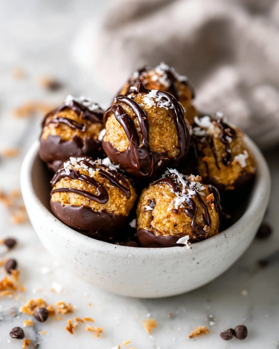 A small white bowl filled with round, bite-sized energy balls that have a light brown base dotted with tiny dark seeds or chocolate bits. Each ball is partially covered in a thick, smooth dark chocolate dip at the bottom, with drizzles of the same dark chocolate on the top surface. The energy balls are topped with small, thin white flakes, possibly coconut, adding texture and color contrast. The bowl sits on a white marbled surface with scattered small chocolate pieces around it, creating a natural and cozy look. Photo taken with an iphone --ar 4:5 --v 7