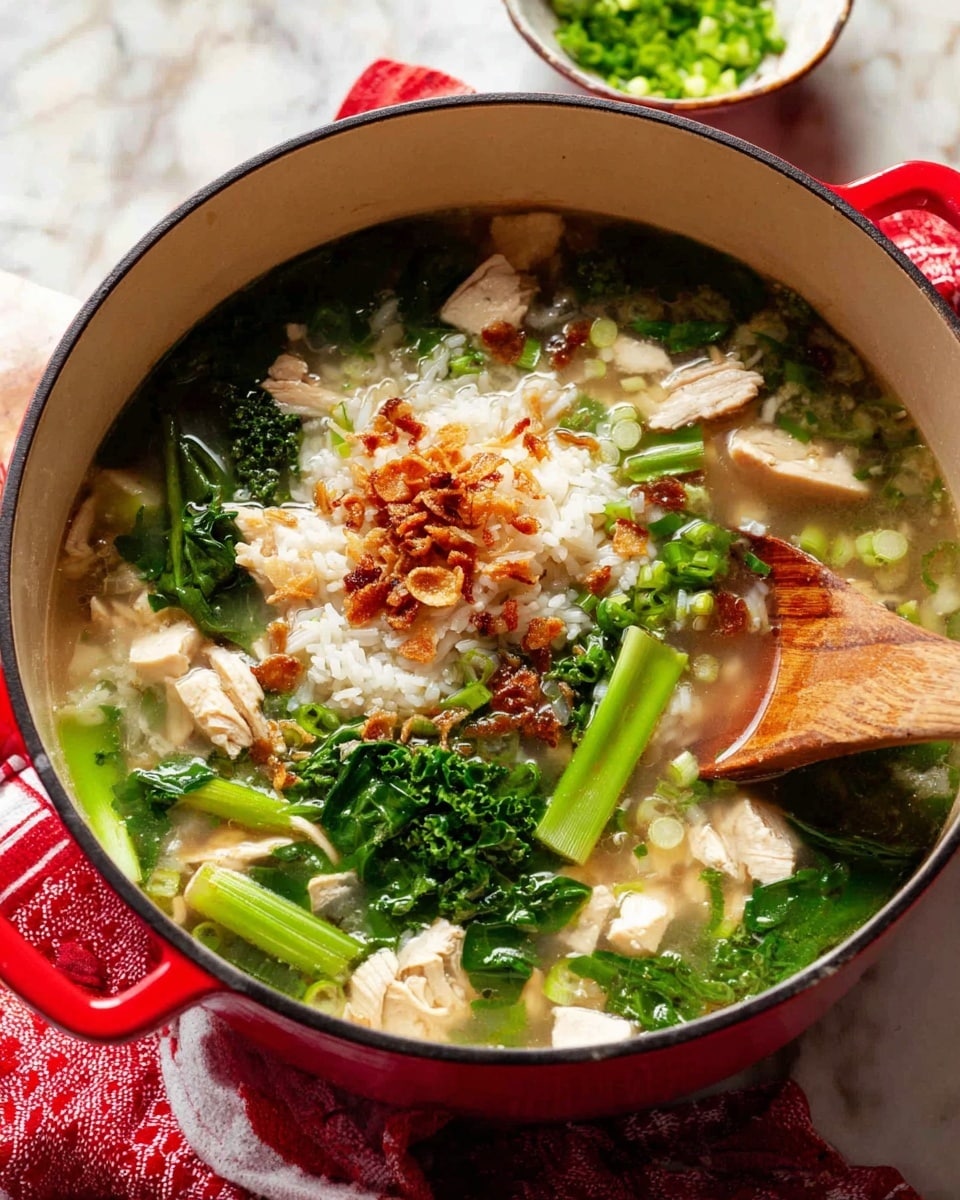 A red pot filled with soup shows several layers inside. The soup has a clear broth covering a layer of white rice near the center with some green leafy vegetables and green stalks scattered around. Pieces of light-colored chicken chunks are spread throughout the soup. On top, there are golden brown fried garlic slices adding crisp texture. A light wooden spoon rests inside the pot on the right side. The pot sits on a surface with a white marbled texture, and a small white bowl with chopped green onions floats blurred in the background. A red and white cloth is partially seen near the pot's handle. Photo taken with an iphone --ar 4:5 --v 7