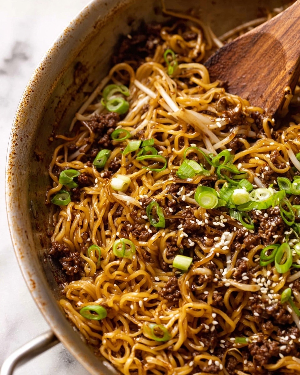 A close-up of a pan filled with cooked noodles mixed with small pieces of dark brown ground meat and light brown bean sprouts. Thin, curly noodles are coated in a shiny sauce giving a rich brown color. Bright green sliced scallions are scattered on top along with small white sesame seeds. A wooden spoon rests inside the pan on the right side, partially stirring the noodles. The pan sits on a white marbled surface. photo taken with an iphone --ar 4:5 --v 7