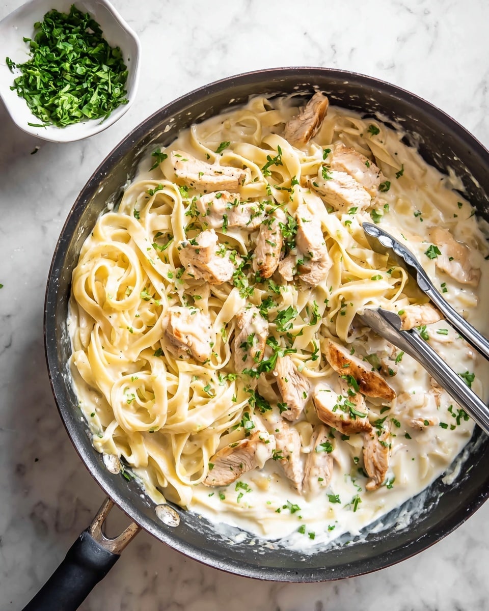 A black pan sits on a white marbled surface, filled with creamy white Alfredo sauce at the bottom. On top of the sauce is a single layer of light yellow fettuccine noodles that look soft and smooth, mixed evenly with thin slices of cooked chicken breast showing a light golden-brown sear. Small bits of bright green chopped parsley are sprinkled all over the pasta and chicken, adding a fresh touch. To the side of the pan, there is a small white bowl filled with more finely chopped parsley. A pair of silver tongs rests on top of the noodles, gently holding some pasta and chicken slices. photo taken with an iphone --ar 4:5 --v 7