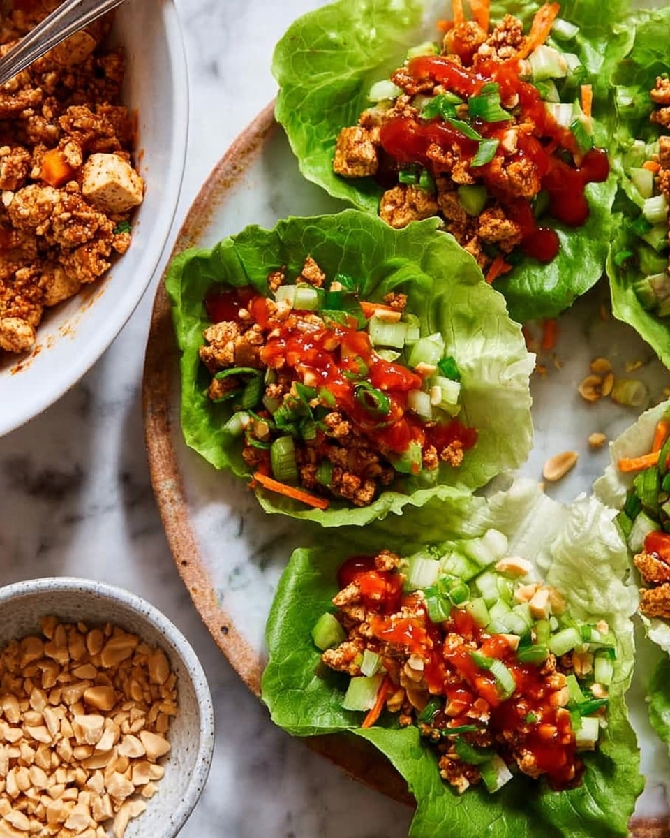 The image shows fresh green lettuce leaves used as wraps, each filled with a colorful mixture of diced tofu or meat, and small chopped vegetables including orange carrots and green peppers. The filling is topped with a bright red sauce drizzled in a wavy pattern, sprinkled with chopped peanuts and chopped green onions, adding texture and brightness. The lettuce wraps are laid out on a white marbled surface near a white bowl containing more of the chopped filling and a small white dish with extra chopped peanuts. The scene is bright and fresh, with a focus on the vibrant colors of the food. photo taken with an iphone --ar 4:5 --v 7