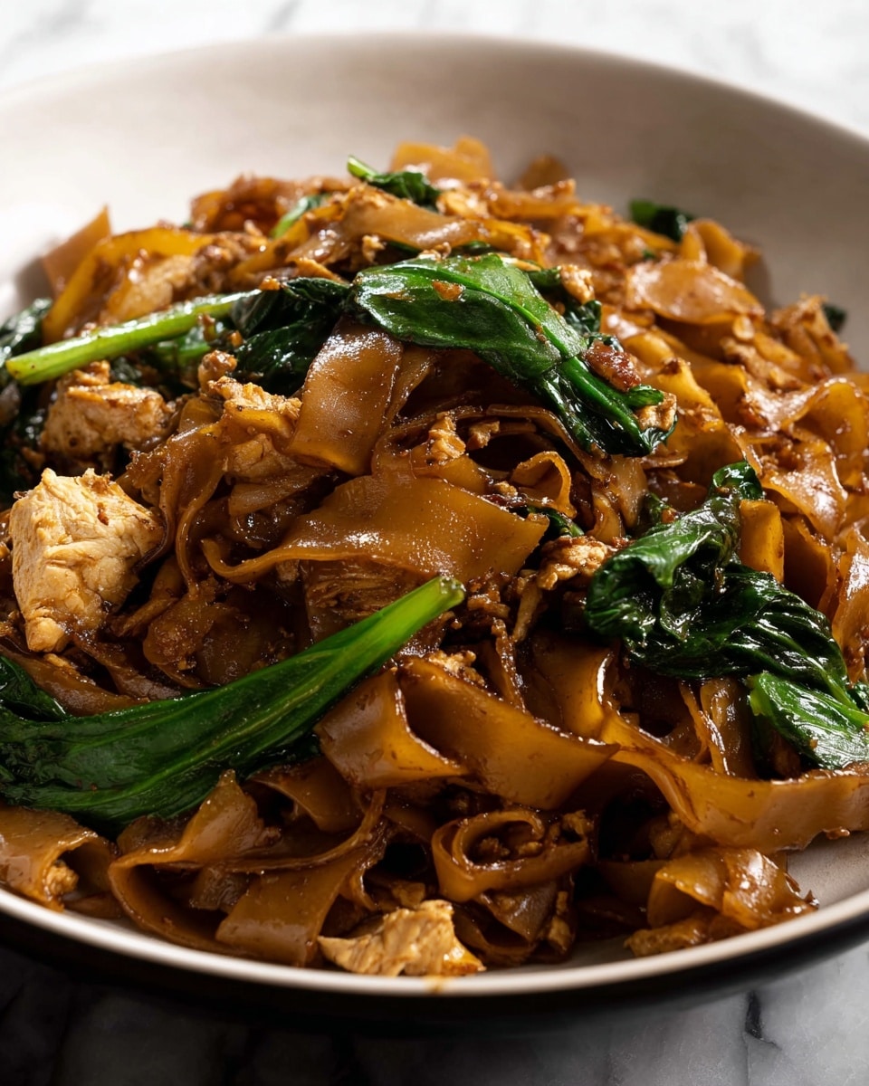 The image shows a close-up of a black bowl filled with a stir-fried noodle dish. The dish has thick, wide, glossy brown noodles that have a slightly curled texture. Mixed within the noodles are small chunks of light brown cooked chicken, bright green leafy vegetables, and pieces of scrambled egg with a pale yellow color. The green vegetables are spread around the noodles, adding color contrast. The noodles and ingredients appear to be coated in a rich brown sauce, giving the dish a shiny and appetizing look. The background has a white marbled texture. photo taken with an iphone --ar 4:5 --v 7
