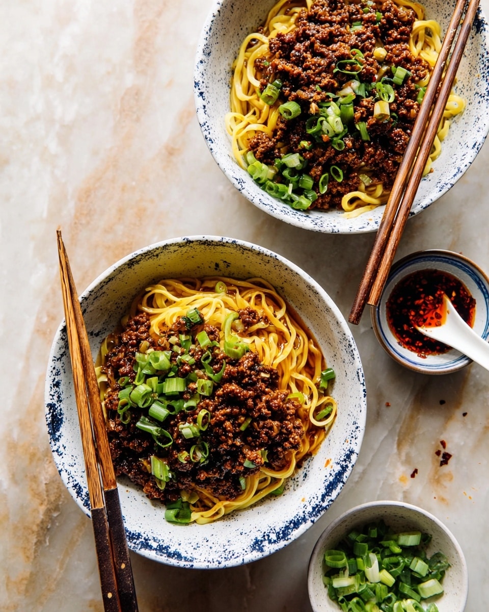 Two white bowls with dark blue patterns are filled with a noodle dish. The bottom layer is yellow noodles sitting in a light brown sauce. On top of the noodles is a layer of cooked minced meat that is dark brown and looks crispy. Bright green sliced scallions are spread over the meat as the top layer, adding freshness and color. Each bowl has a pair of wooden chopsticks resting on the edge with blue and white decorated handles. Around the bowls, some sliced scallions are scattered on a white marbled surface. Nearby, a small white dish holds more scallions, and another small white dish contains a spoon filled with red chili oil and a garlic clove. photo taken with an iphone --ar 4:5 --v 7