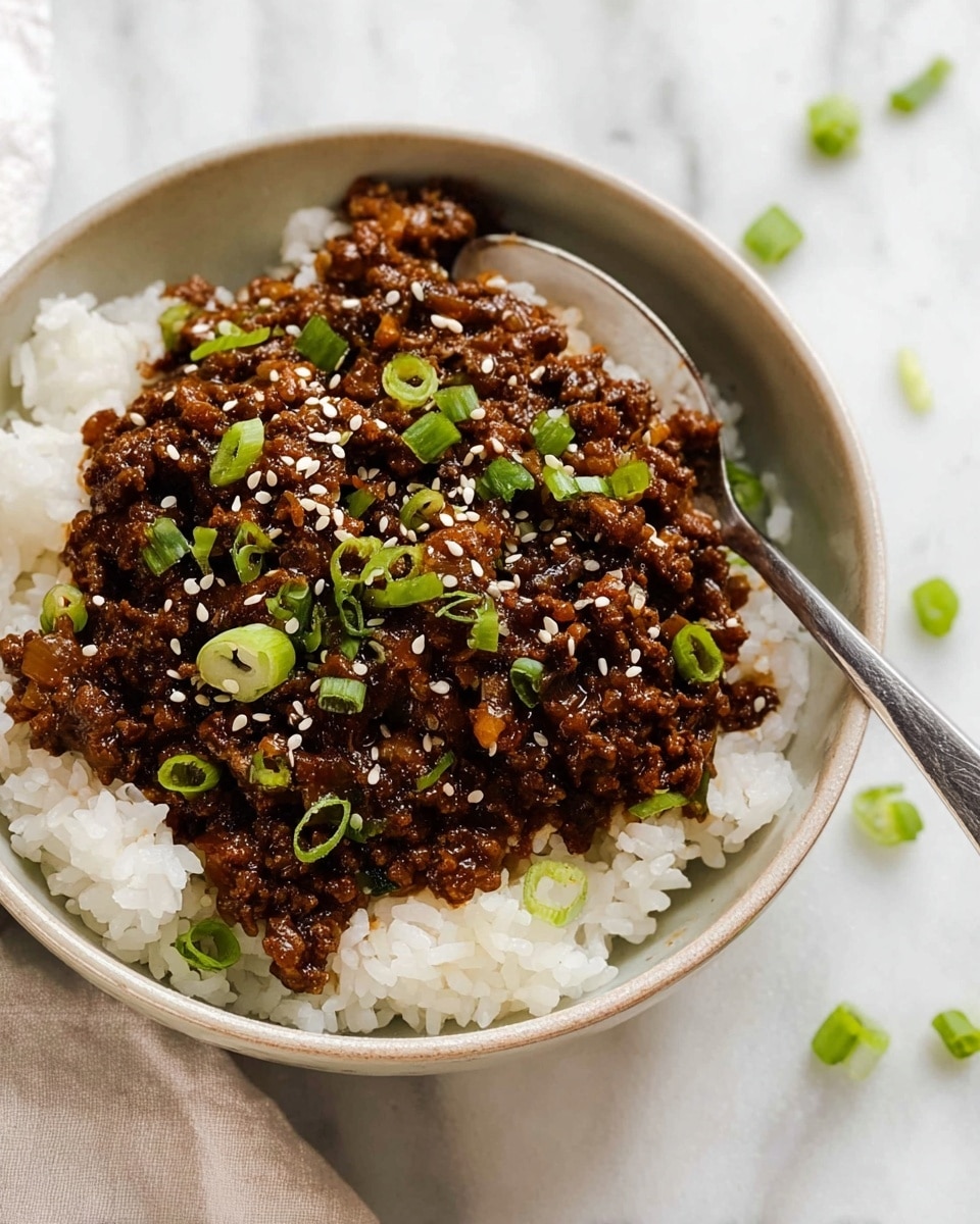 A white bowl shows two layers, the bottom one is fluffy white rice with a soft texture, topped with a rich dark brown cooked ground beef mixed with small pieces of onions. The beef looks juicy and sits heaped on the rice, sprinkled with small white sesame seeds and bits of bright green chopped spring onions. A silver spoon rests inside the bowl, slightly lifting some of the beef. The bowl is placed on a white marbled surface with a few scattered green onion rings around. photo taken with an iphone --ar 4:5 --v 7