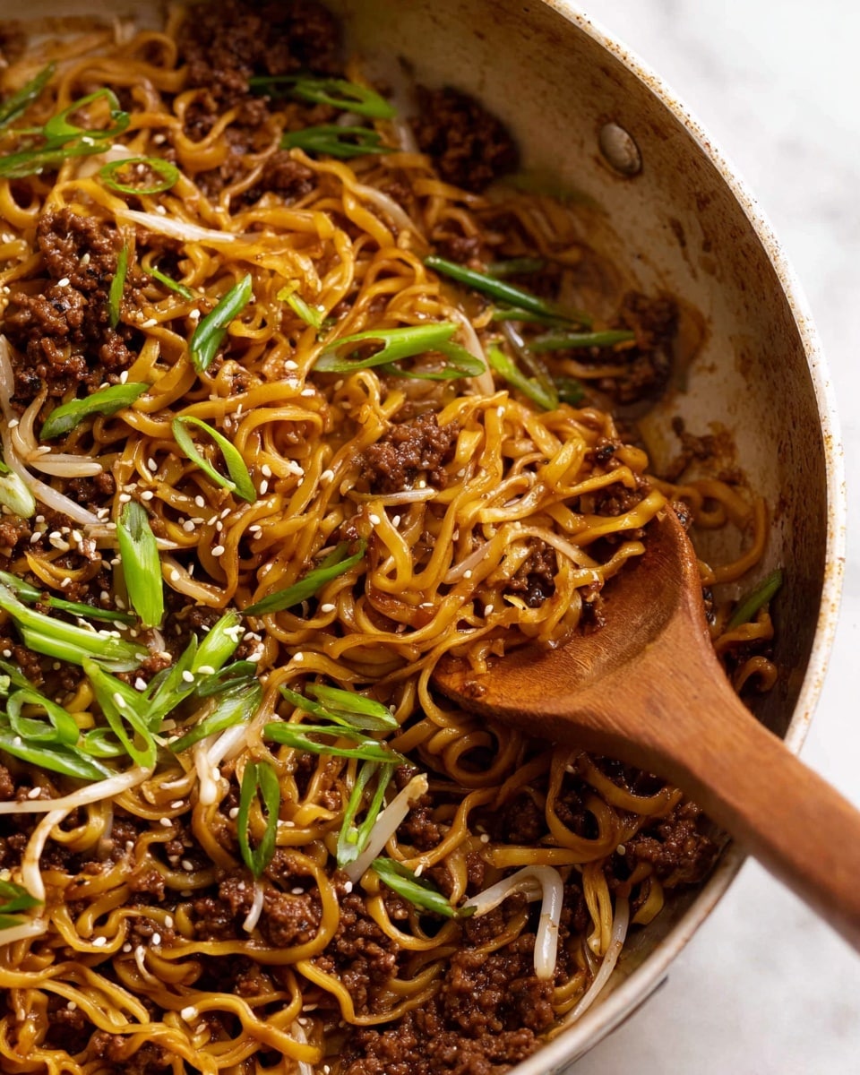 A close-up view of a round pan filled with stir-fried noodles showing three main layers: the bottom layer has curly, golden-brown noodles mixed with slightly translucent bean sprouts, the middle layer is made of small, dark brown pieces of cooked ground beef scattered throughout, and the top layer is garnished with bright green sliced scallions and sprinkled white sesame seeds. A wooden spoon is partially visible on the right side, mixing the ingredients on a white marbled surface. photo taken with an iphone --ar 4:5 --v 7