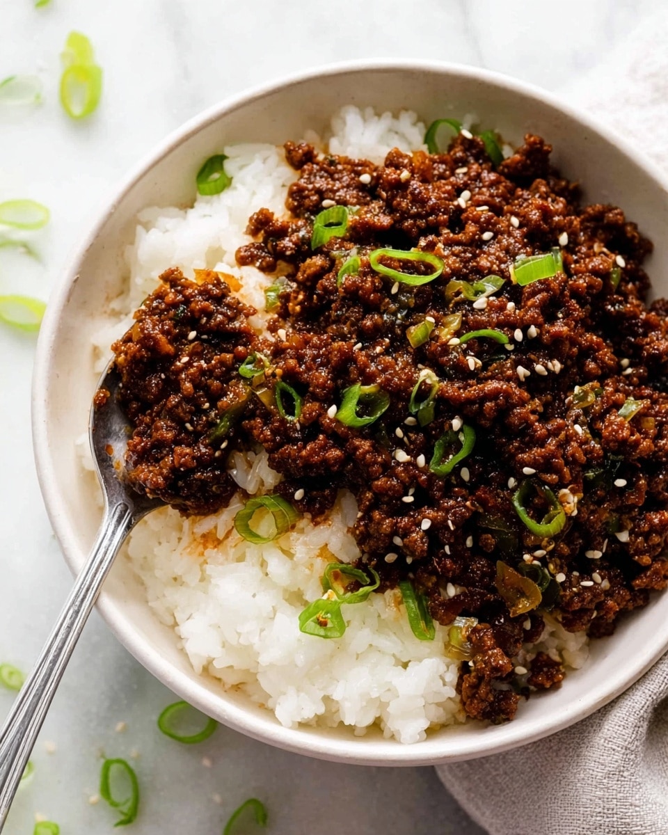 A bowl with a bottom layer of white rice, looking soft and fluffy, topped with a thick layer of dark brown ground beef mixed with small cooked onion pieces. The beef mixture is garnished with white sesame seeds and chopped green onions scattered on top and around the dish. A silver spoon is resting inside the bowl. The bowl sits on a white marbled surface with some green onion pieces scattered nearby. Photo taken with an iphone --ar 4:5 --v 7
