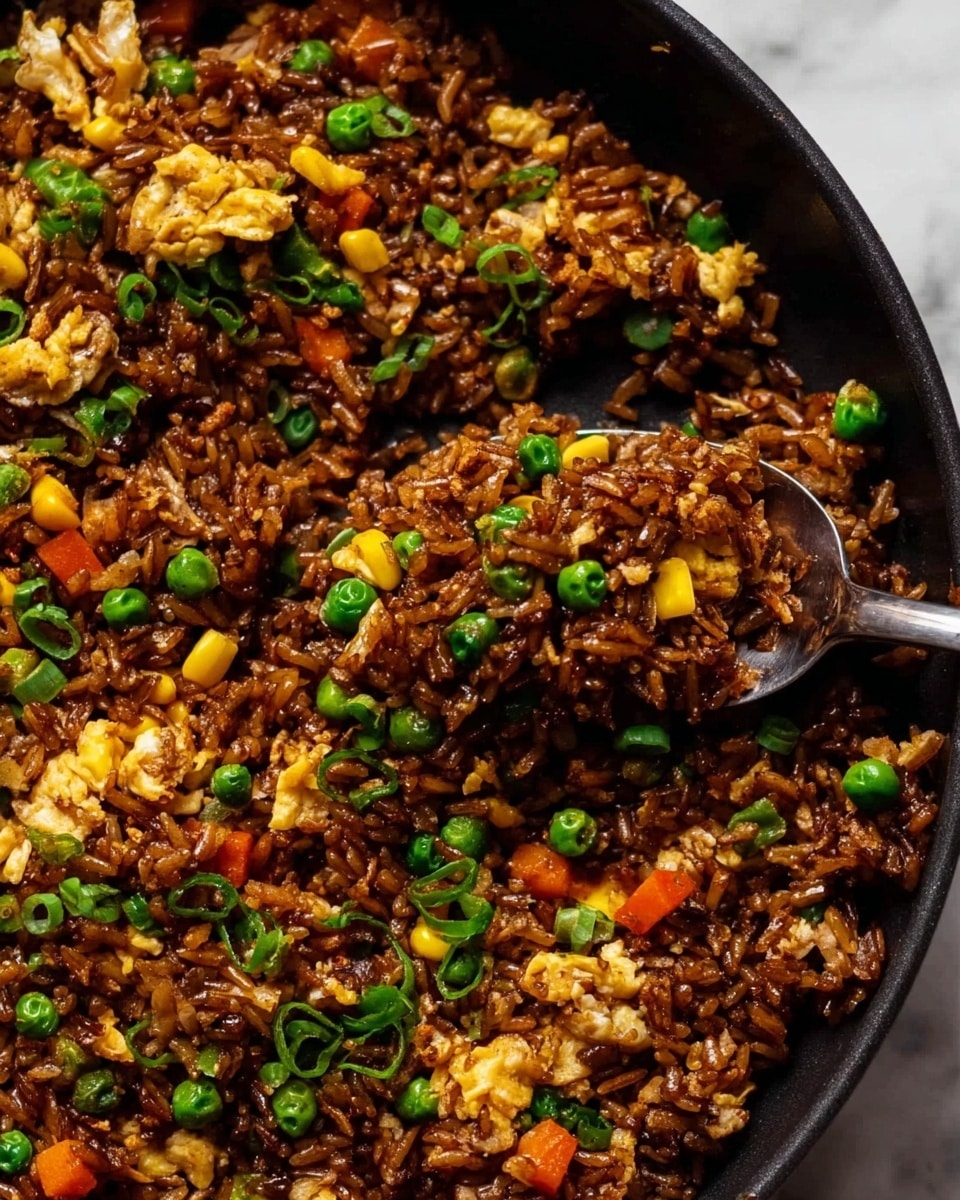 This image shows a close-up of fried rice with mixed vegetables and small pieces of scrambled egg. The dish has three main layers: the base is made of dark brown seasoned rice, mixed throughout with bright yellow corn kernels, soft green peas, and small red bell pepper cubes. On top, there are light yellow bits of scrambled egg scattered unevenly. The rice grains look shiny and slightly oily, with some chopped green onions sprinkled over it, adding a fresh green touch. A metal spoon scoops a portion of the fried rice, lifting it above the white marbled surface. The photo taken with an iphone --ar 4:5 --v 7