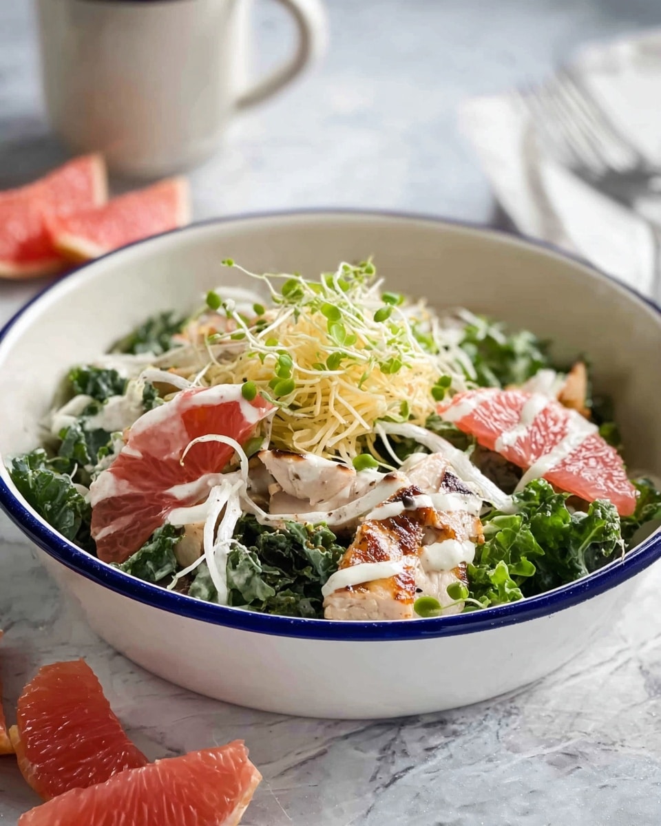 A bowl with a white base and blue rim holds a fresh salad arranged in layers. The bottom layer includes mixed dark green kale leaves and lighter green lettuce. On top are small pieces of grilled chicken with light brown edges, pink grapefruit segments, thin slices of white onion, and thin red onion slices. A creamy dressing is drizzled over, and thin white shredded cheese and green sprouts finish the top. The bowl sits on a white marbled texture surface, with more grapefruit segments placed nearby and a white cup with a blue rim in the background. Photo taken with an iphone --ar 4:5 --v 7